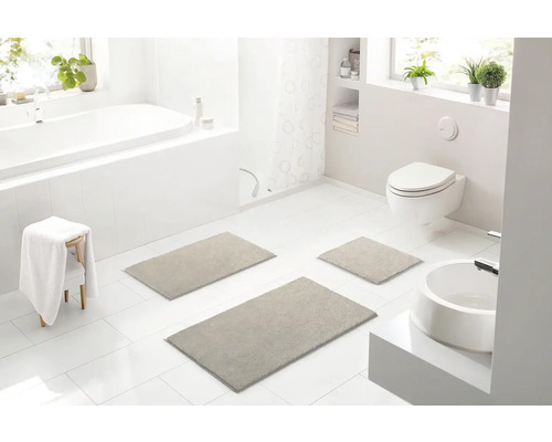 Světlá koupelna s vanou, toaletou, umyvadlem a sadou tří koupelnových předložek