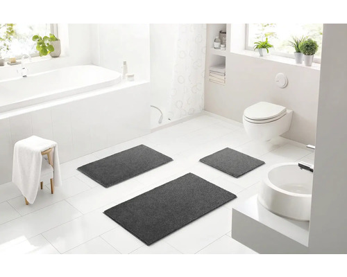 Světlá koupelna s vanou, toaletou, umyvadlem a sadou tří šedých koupelnových předložek