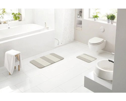 Světlá koupelna s vanou, umyvadlem, toaletou a pruhovanými koupelnovými předložkami