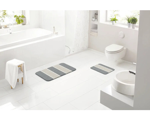 Koupelna s vanou, umyvadlem, toaletou a dvěma pruhovanými koupelnovými předložkami.