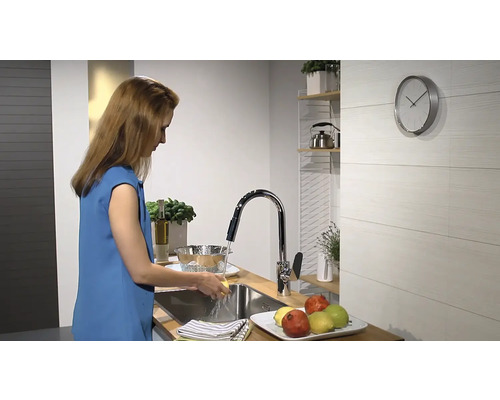 Žena myje zeleninu pod kohoutkem v moderní kuchyni