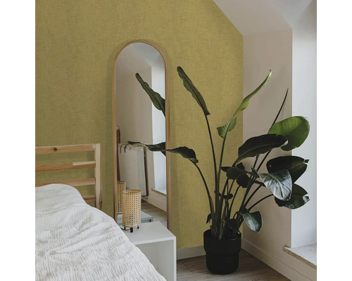 Ložnice s postelí, zrcadlem a pokojovou rostlinou před strukturovanou tapetou