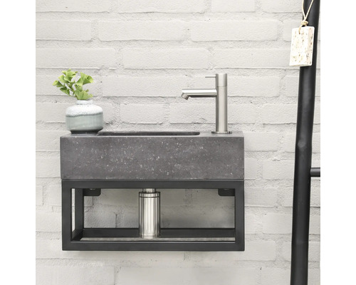 Moderní umyvadlo se šedým kamenným vzhledem a černým kovovým rámem na bílé cihlové zdi