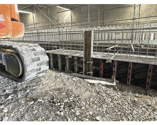 Stavební jáma s bedněním a armovacím železem, pásové rypadlo v popředí.