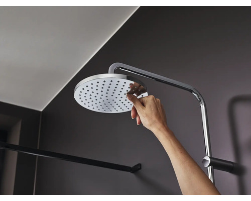 Ruka se dotýká sprchové hlavice se sprchovým ramenem v koupelně