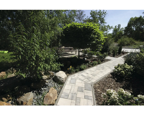 Zahradní cesta s dlažebními kostkami, obklopená stromy a keři