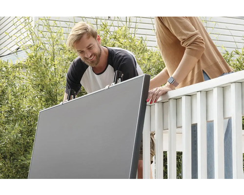 Dvě osoby instalují pomocí svorek plastovou zástěnu na balkon.