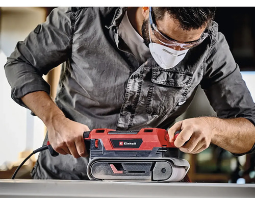 Muž používá pásovou brusku Einhell k broušení dřeva.