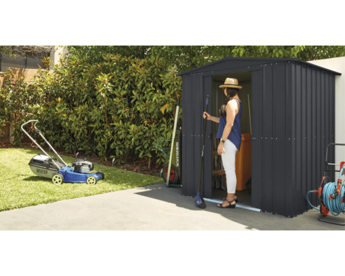 Zahradní scéna se sekačkou na trávu a zahradním domkem, ve kterém stojí žena