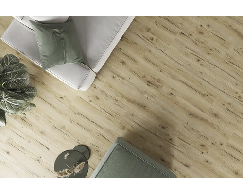 Pohled na místnost s laminátovou podlahou s dřevěným vzhledem, pohovkou, ozdobnými polštáři, pokojovou rostlinou a příručním stolkem.