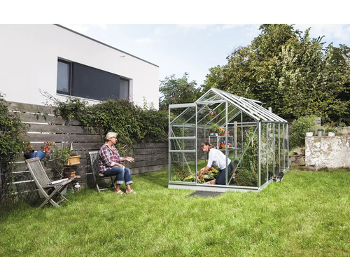 Skleník v zahradě se dvěma ženami, jedna zahradničí, druhá sedí.