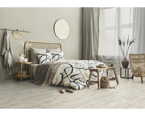 Světlá ložnice s postelí, dřevěným odkládacím stolkem a ratanovým křeslem