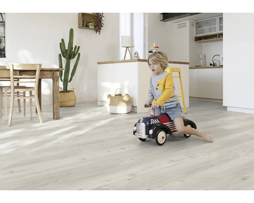 Světlý obývací pokoj s dřevěným stolem, kaktusem, chlapcem na autíčku a světlou dřevěnou podlahou.