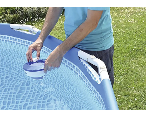 Osoba plní dávkovač bazénové chemie v nadzemním bazénu