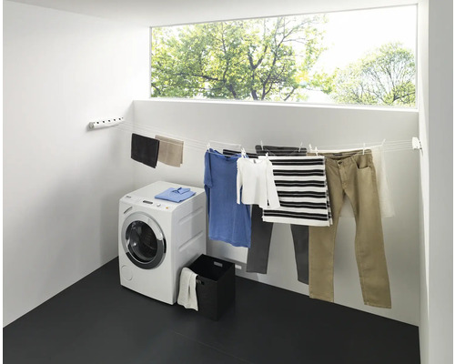 Sušák na prádlo s prádlem, pračka a okno ve světlé místnosti