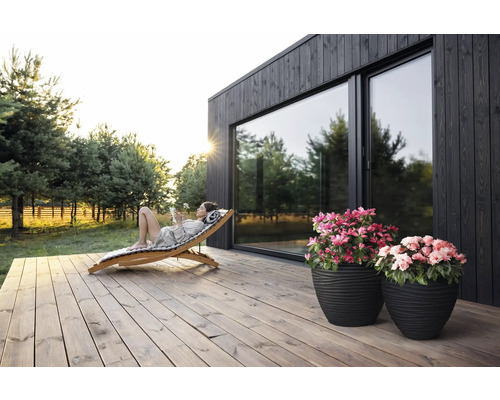 "Scéna s ženou odpočívající na dřevěném lehátku na dřevěné terase před domem s velkými okny