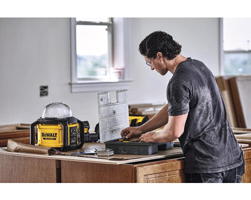 Řemeslník třídí nástroje v bedně na nářadí. V pozadí je pracovní lampa značky Dewalt.