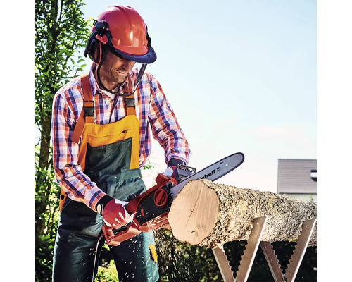 Muž řeže dřevo motorovou pilou a má na sobě ochranný oděv