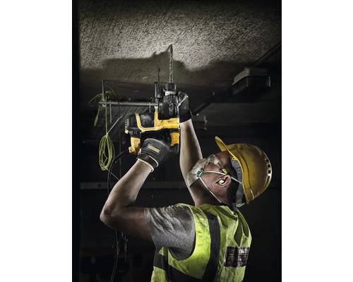 Muž vrtá žlutou vrtačkou do stropu. Má na sobě ochrannou helmu a brýle.