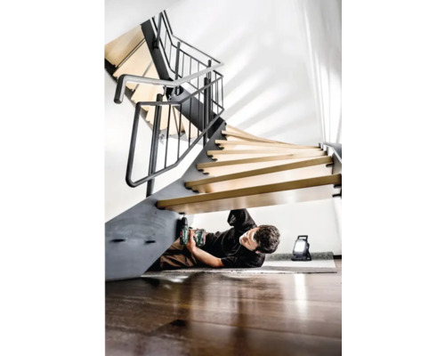 Muž montuje točité schodiště pomocí akumulátorové vrtačky a pracovního světla