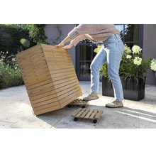 Osoba pohybuje dřevěným květináčem na kolečkové desce v zahradě.