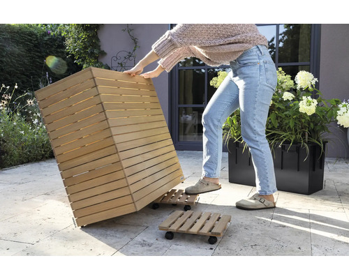 Osoba pohybuje dřevěným květináčem na kolečkové desce v zahradě.
