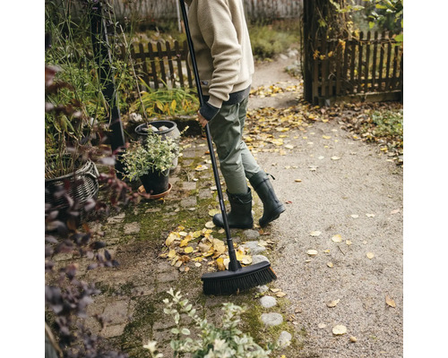 Osoba zametá listí koštětem na ulici na zahradě.