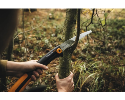 Osoba řeže větev ruční pilou.