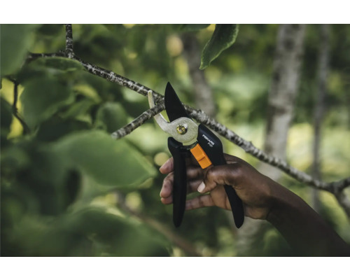 Ruka stříhá větev zahradními nůžkami Fiskars.