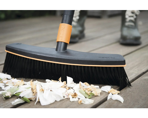 Koště na čištění dřevěné terasy se zbytky rostlin.