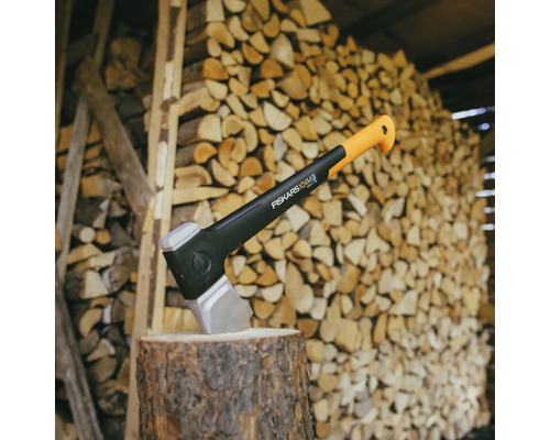 Štípací sekera Fiskars na špalku před hromadou dřeva