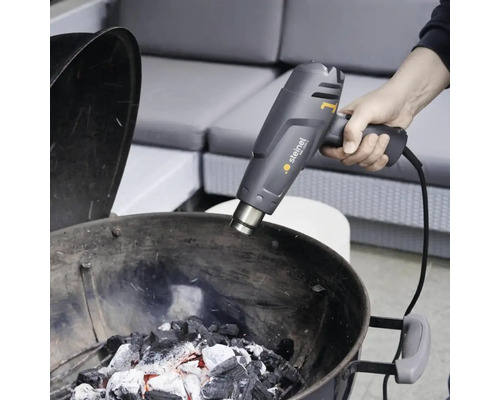 Osoba zapaluje dřevěné uhlí pomocí horkovzdušné pistole Steinel.