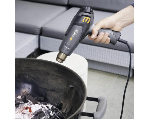 Osoba zapaluje dřevěné uhlí v grilu horkovzdušnou pistolí.