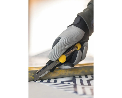 Ruka v pracovní rukavici používá nůž na řezání materiálu.