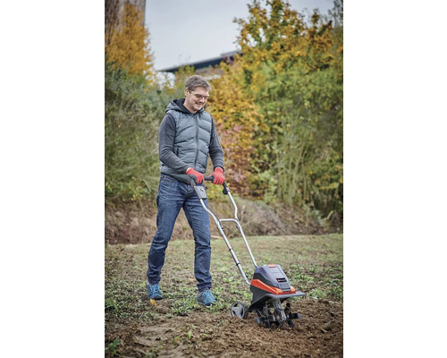 Muž používá motorový kultivátor pro zpracování půdy na zahradě.