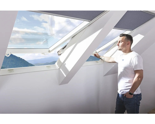 Muž otevírá střešní okno s výhledem ven