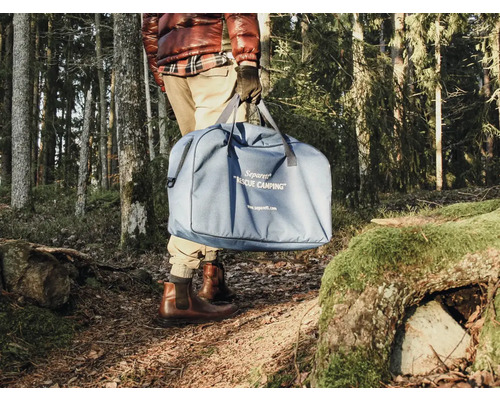 Osoba nese modrou kempingovou toaletu v tašce v lese