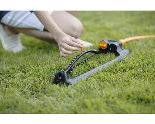 Osoba nastavuje regulátor na zavlažovači trávníku, který stojí na trávníku.