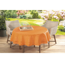 Zahradní stůl s oranžovým ubrusem a ratanovými židlemi venku.