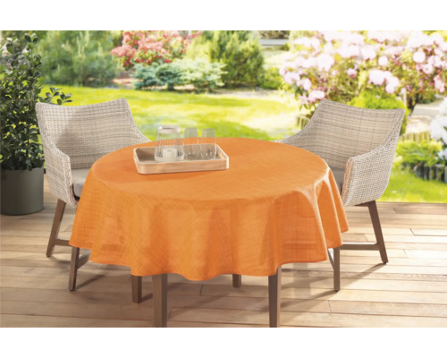 Zahradní stůl s oranžovým ubrusem a ratanovými židlemi venku.