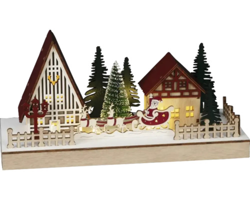Dekorativní vánoční krajina s domy, jedlemi, soby a Santa Clausem na saních