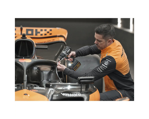 Muž připevňuje něco k závodnímu vozu pomocí akumulátorového šroubováku.