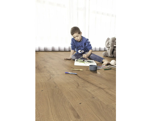 Dítě maluje na dřevěné podlaze. V pozadí je plyšový slon.