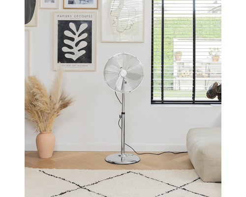 Stříbrný ventilátor na podlaze pokoje s kobercem a uměleckými díly.