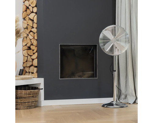 Obývací pokoj s krbem, palivovým dřívím a stojacím ventilátorem