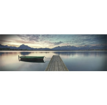 Klidné jezero s dřevěným molem a malou lodí v popředí, s horskou krajinou v pozadí.