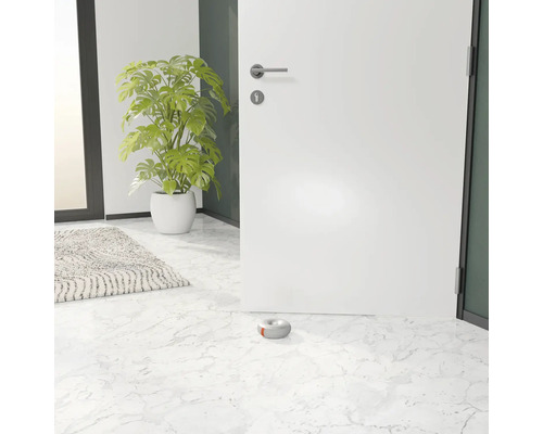 Otevřené bílé dveře s šedým dveřním dorazem na mramorové podlaze