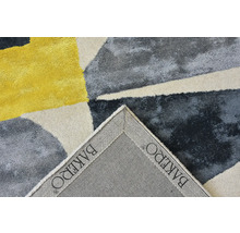 Detailní pohled na koberec s geometrickým vzorem a ohnutým rohem zobrazující BAKERO Logo na rubové straně.