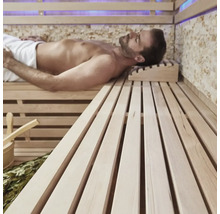 Muž relaxuje v sauně s dřevěnými lavicemi a příslušenstvím.