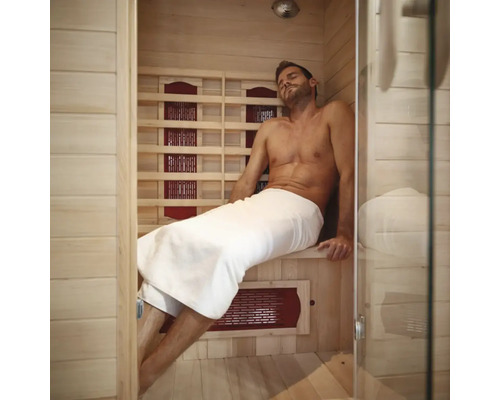 Muž relaxuje v infračervené sauně s dřevěnými stěnami a skleněnou přední stranou